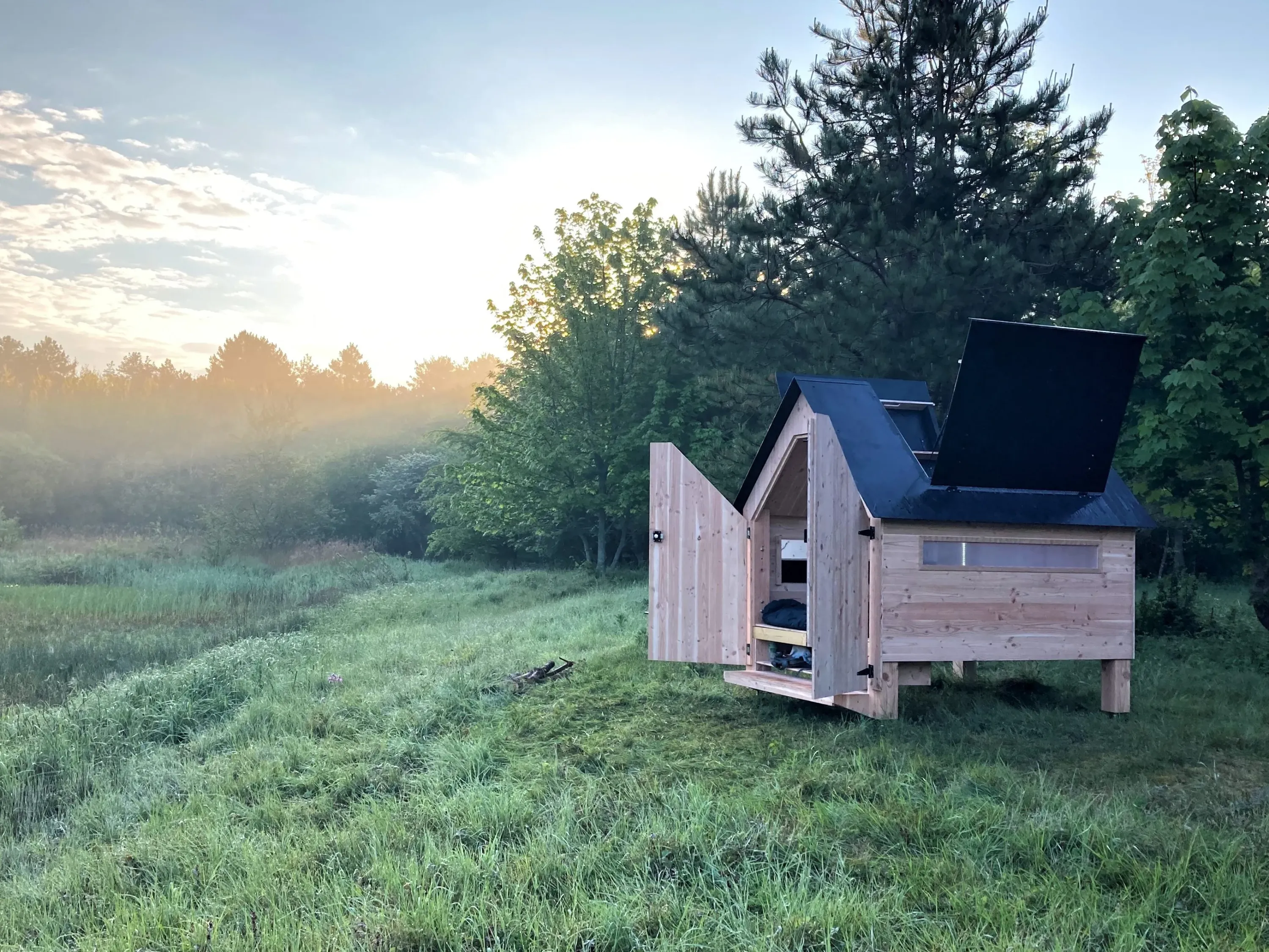Cabane Hut'Op ouverte dans un champ vert lors d'un coucher de soleil